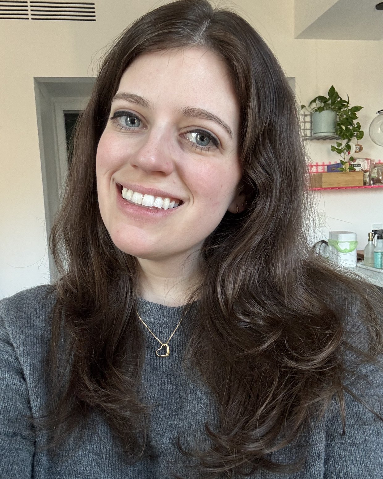Sara Birchard smiling, wearing a grey sweater and a gold heart necklace
